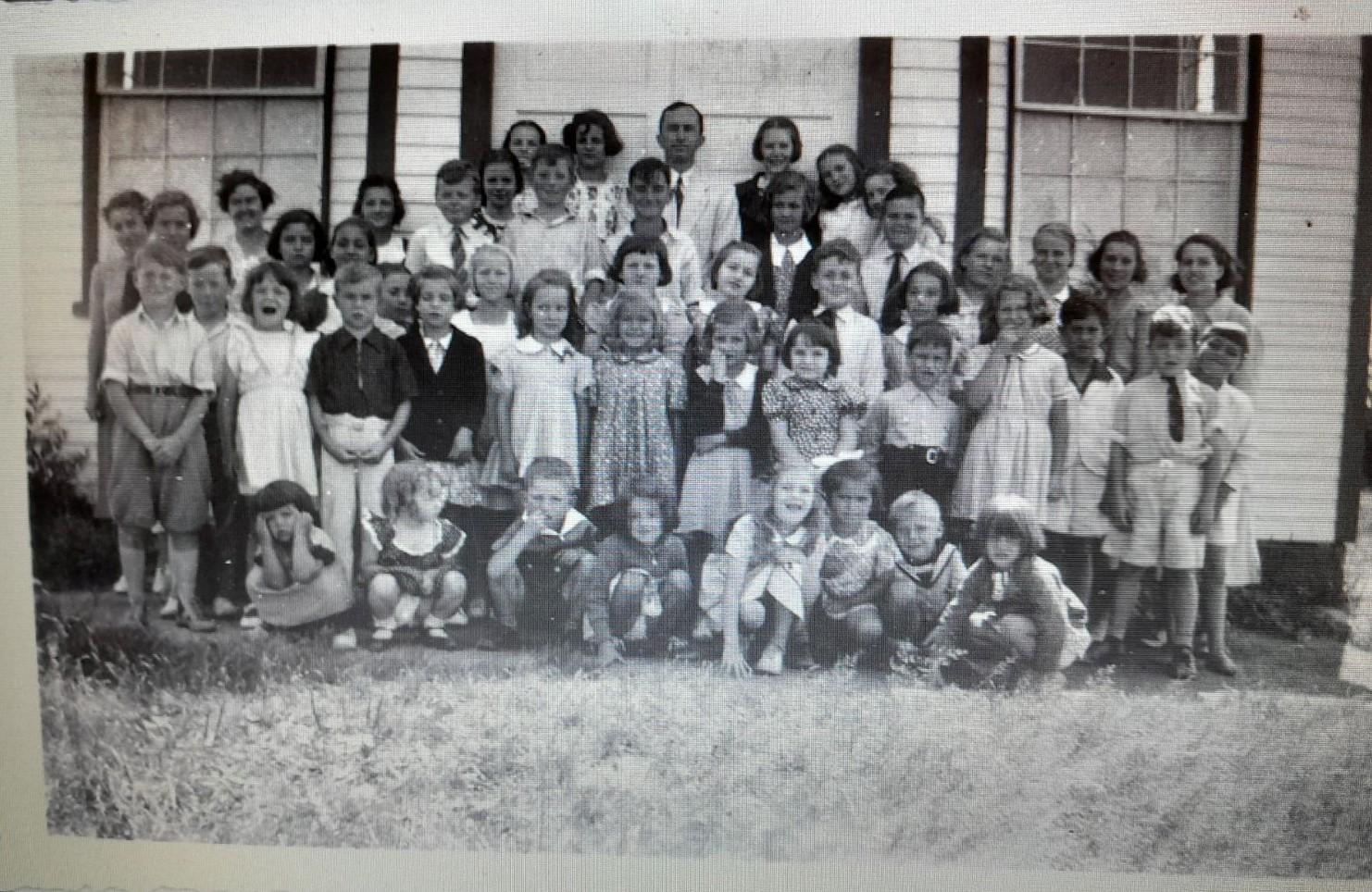 Black and white photograph of large group of children standing in front of a white building
