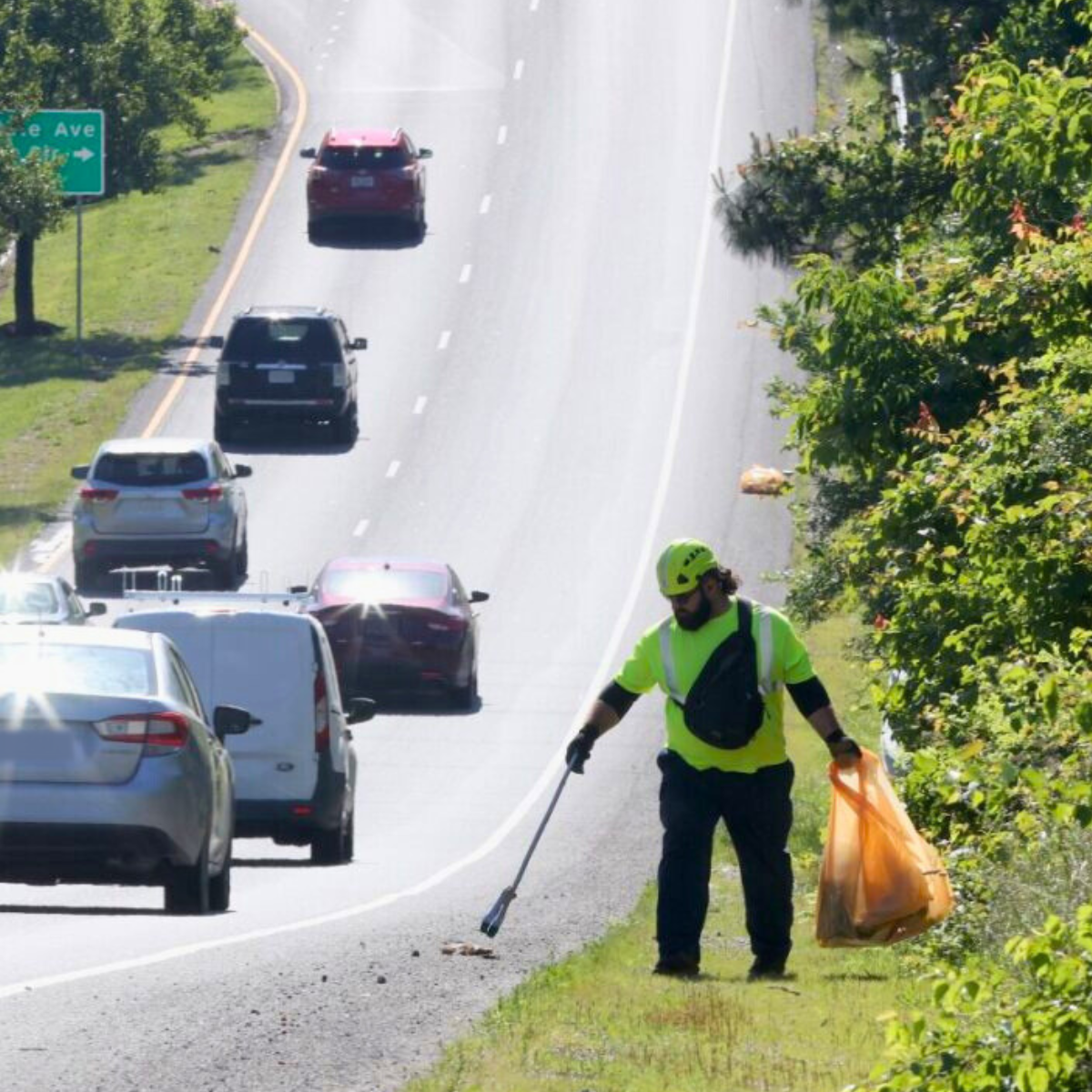 Man picking up litter from roadway as cars drive by.