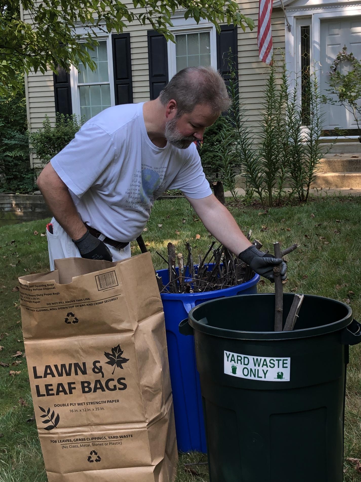 Man placing yard waste and small branches into container labeled "Yard Waste".